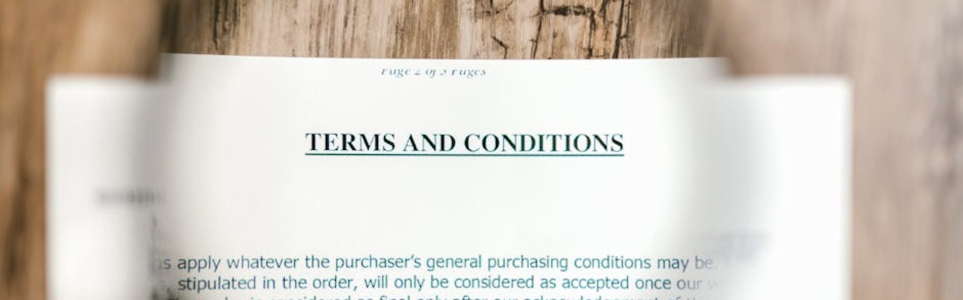 Magnifying glass focusing on terms and conditions document on wooden surface.